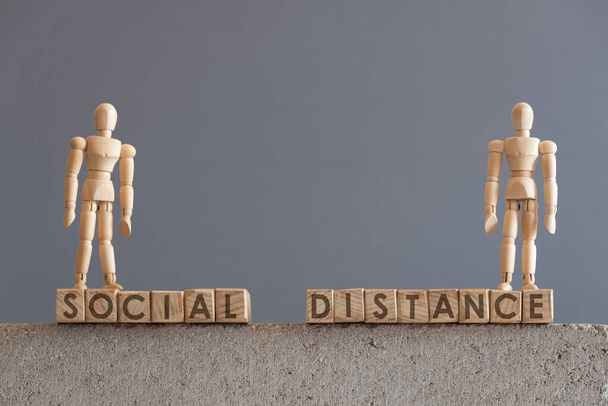 Conceptual image about social distancing, mandatory due to the coronavirus outbreak, covid-19. Pair of wooden human figures standing on cubes with the text Social Distance - Photo, Image
