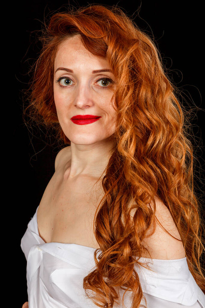 Όμορφη κοπέλα με κόκκινα μαλλιά σε λευκό πουκάμισο και καπέλο σε μαύρο φόντο γκρο πλαν - Φωτογραφία, εικόνα