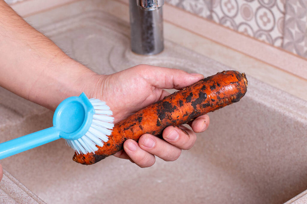 As mãos lavam cenouras na pia na cozinha
 - Foto, Imagem