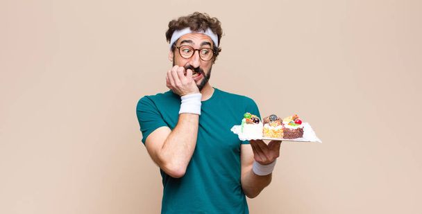 young sports man with cakes against flat wall - Valokuva, kuva