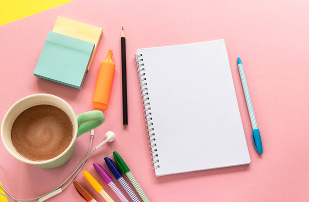 Sketch pad (notebook), multi colored pens, mug with coffee and headphones on the pink background. Stationery in top view design with text space. - Photo, image