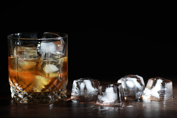 Un vaso de bebida alcohólica fuerte con hielo en barra de madera. Whisky con hielo. Vaso con una bebida fría. - Foto, Imagen