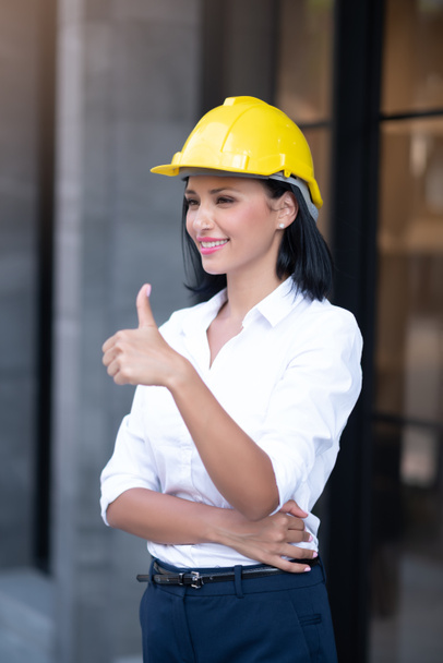 Portrait of Smart Business Woman Civil Engineer and Architecture Wearing Yellow Helmet Hard Hat and Showing Thumbs Up While Standing in Business Building Project with Confidence Poses - Photo, Image