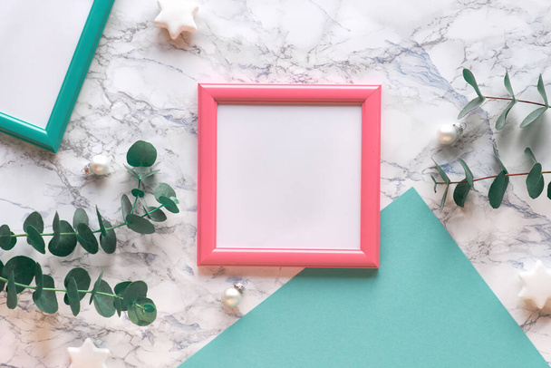 Christmas frame in salmon pink and mint green. Fresh eucalyptus twigs and white and white glass Xmas trinkets. Flat lay, top view on white marble background with copy-space in frame. - 写真・画像