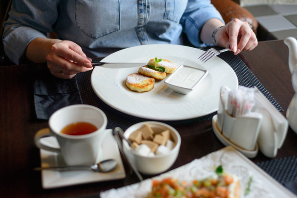 Reggeli vagy reggeli az étteremben. asztal italokkal és étellel. A nők kezei késsel és villával vágják a sajttortát. szelektív fókusz - Fotó, kép