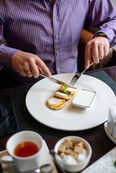 πρωινό ή brunch στο εστιατόριο. τραπέζι με ποτά και φαγητό. άνθρωπος χέρια κομμένα cheesecakes με ένα μαχαίρι και πιρούνι. επιλεκτική εστίαση - Φωτογραφία, εικόνα