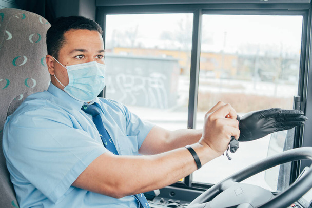 el conductor del autobús del hombre latino tiene la máscara azul de la protección médica pone guantes negros en sus manos para protegerse de la epidemia del coronavirus, covid 19. protege del virus de la corona. cuarentena 2020
 - Foto, imagen