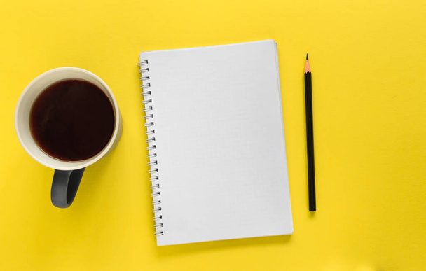 Notebook, pencil and mug of coffee (tea) on the yellow background. To do list. Flat lay design with copy space. - Foto, afbeelding