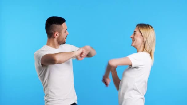 Couple of young happy man and woman dancing together on blue background at studio. Fun, relationship and emotions concept - Filmati, video