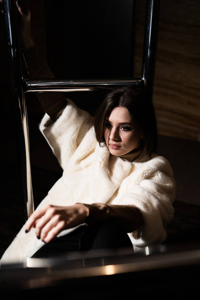 Sexy brunette girl sit on hotel luggage cart. Luggage Trolley at the hotel. Glamorous young woman wearing stylish white fur coat. Fashion, fur, hotel, travel and beautiful people concept.. - Photo, Image