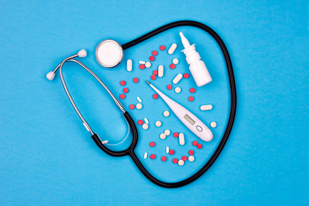 Борьба с вирусом - фонендоскоп, термометр и медицина. Капсулы и таблетки, спрей для носа на синем фоне
 - Фото, изображение