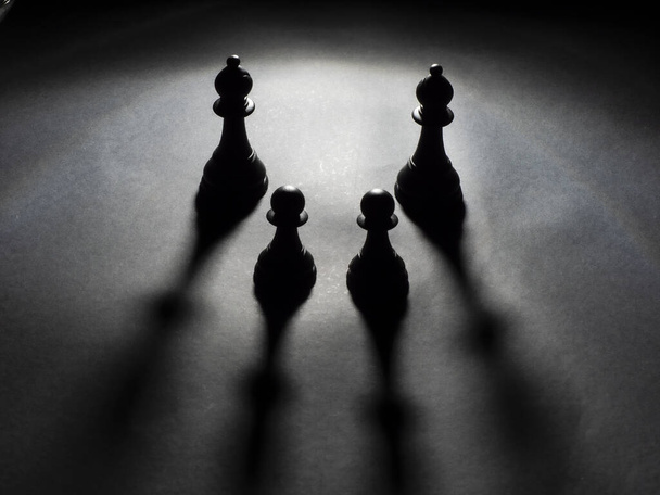 Image of two black bishops and two black pawns backlighting with black background - Photo, Image