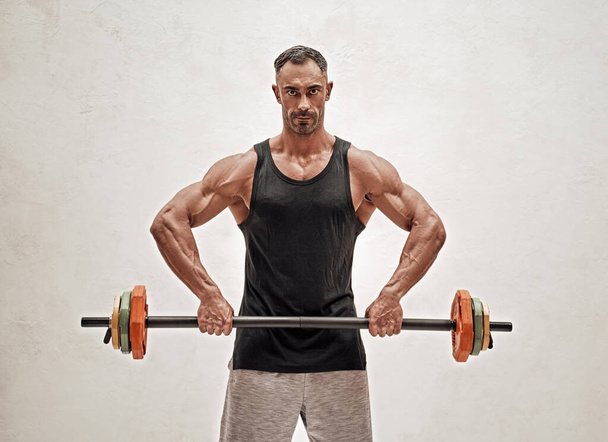 Brutale spieropbouwer die spieren oppompt met lange halter op een witte achtergrond. Workout bodybuilding concept. - Foto, afbeelding