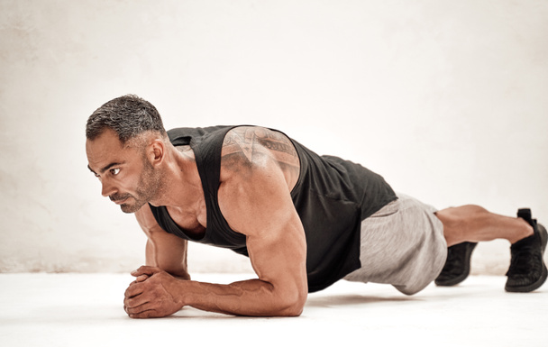 Спортивний дорослий білий чоловік робить дошку вправи для своїх абс і м'язів спини, дивлячись зосереджено в яскравій студії
 - Фото, зображення