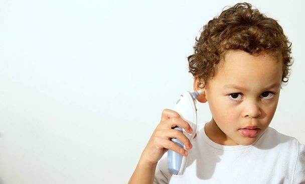 bambino che controlla la sua temperatura con un termometro auricolare - Foto, immagini