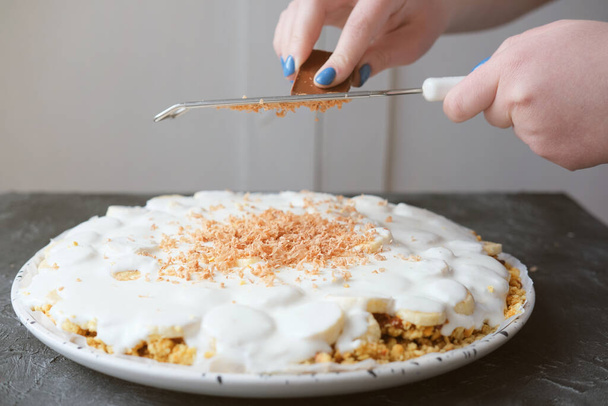  woman's hands grating chocolate on Banoffee pie with bananas, whipped cream, chocolate and toffee. homemade banoffee pie. - Foto, imagen