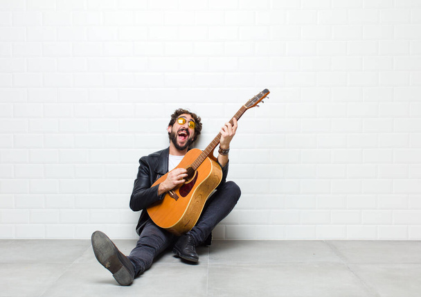 junger Mann mit Gitarre auf dem Boden sitzend - Foto, Bild