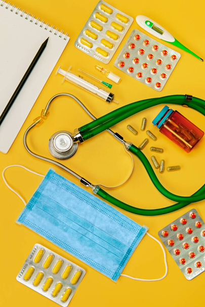 Concept, of medical equipment, flat lay top view. A medical mask, drugs and stethoscope on a yellow background. Health checkup or health insurance lung diagnosis, coronavirus, diagnosis of pneumonia. - Photo, Image