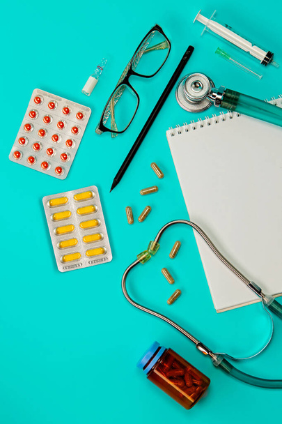 A stethoscope, thermometer, pills, notepad and glasses on doctor table or nurse desk. Concept of lung diagnosis, coronavirus, diagnosis of pneumonia. Flat lay top view. Copy space for text - Photo, Image