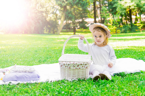 Une petite belle fille se promène dans le parc avec un panier de pique-nique et un chapeau de paille. Bébé émotionnel drôle. - Photo, image