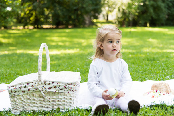 Mała piękna dziewczynka spaceruje po parku z koszykiem piknikowym i słomkowym kapeluszem. Zabawne emocjonalne dziecko.. - Zdjęcie, obraz