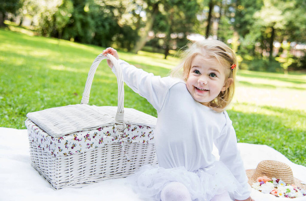 Malá krásná holčička chodí do parku s piknikovým košem a slamákem. Vtipné emocionální dítě. - Fotografie, Obrázek