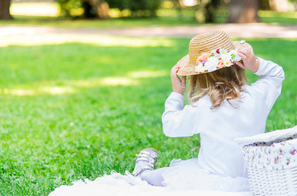 Mała piękna dziewczynka spaceruje po parku z koszykiem piknikowym i słomkowym kapeluszem. Zabawne emocjonalne dziecko.. - Zdjęcie, obraz
