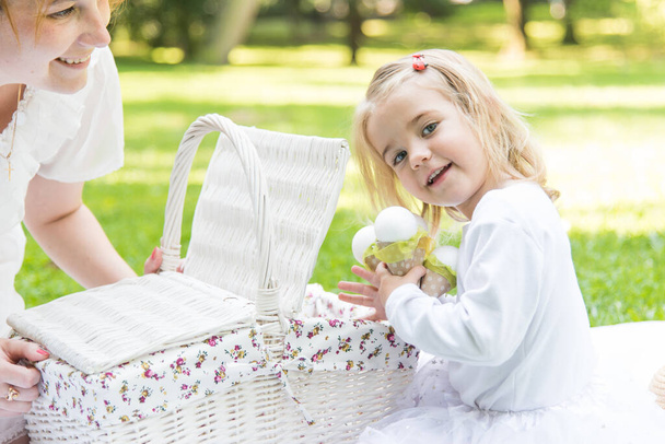 A little beautiful girl walks in the park with a picnic basket and straw hat. Funny emotional baby. - Photo, Image