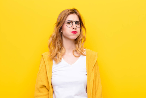 young pretty blonde woman with a goofy, crazy, surprised expression, puffing cheeks, feeling stuffed, fat and full of food against yellow wall - Foto, immagini
