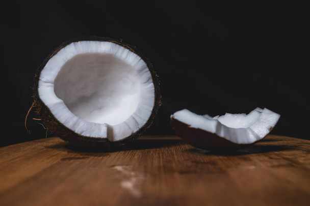 Split coconut is lying on a wooden Board. Tasty tropical fruit. healthy nutrition. Diet concept. Concept design. Closeup of coconut. Healthy fresh nutrition. Vegetarian healthy food. Dark background. #LockdownArt - Fotó, kép