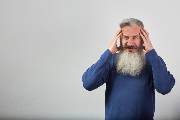 Retrato de hombre barbudo de pelo gris maduro en sudadera azul con dolor de cabeza sobre fondo gris, enfoque selectivo
 - Foto, Imagen