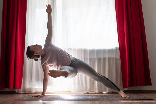 Blanke vrouw doet Vasisthasana variatie of Side Plank yoga pose thuis. - Foto, afbeelding