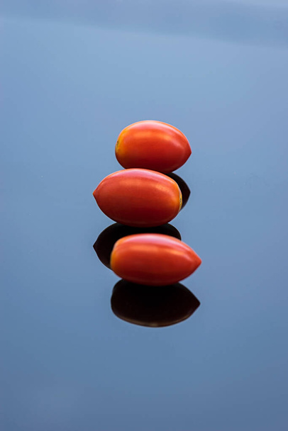Ντομάτες κόκκινες με την αντανάκλασή τους σε μια καταγάλανη γυάλινη επιφάνεια. - Φωτογραφία, εικόνα