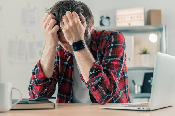 Disappointed freelancer at home office with his head in hands, selective focus - 写真・画像
