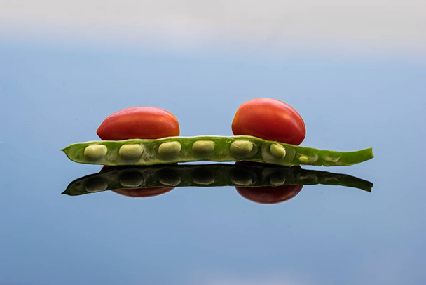 Frijol verde y tomates cherry rojos en una superficie limpia de vidrio azul con reflejos y sombras
. - Foto, imagen