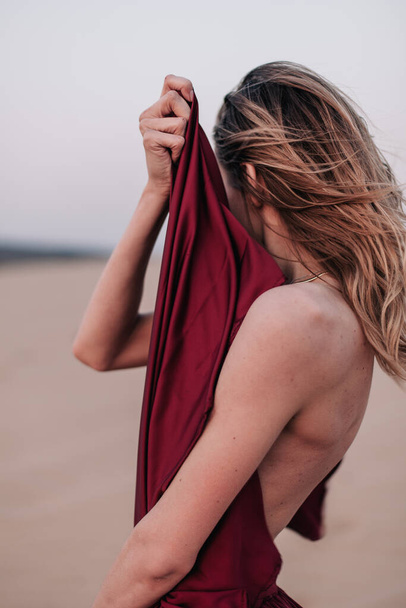portrait of a young slender girl in a red dress in the wind in the desert - Foto, imagen