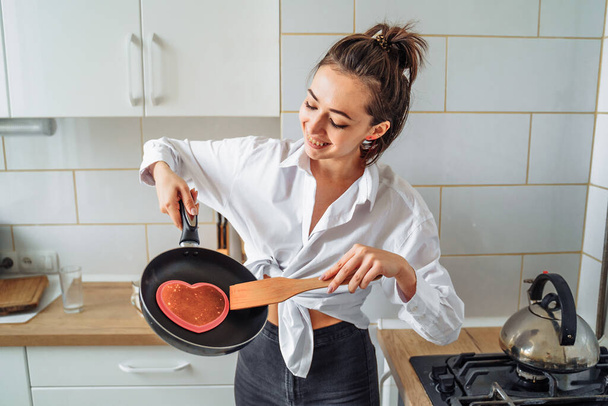 Homemade woman likes to cook delicious desserts from natural products. Making banana pancakes, turning over by wooden spatula the already fried side of the fritters in the pan. Heart and star pancakes - Fotó, kép