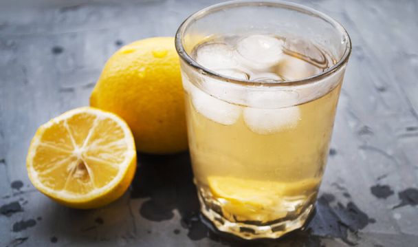 Limonata fatta in casa con ghiaccio in un bicchiere. Vetro, limoni e gocce su sfondo grigio
. - Foto, immagini