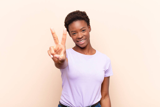 young pretty black womansmiling and looking happy, carefree and positive, gesturing victory or peace with one hand - Фото, изображение