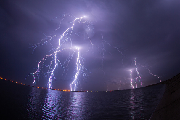 Onweer en bliksemschichten in nacht over een meer met reflaction - Foto, afbeelding