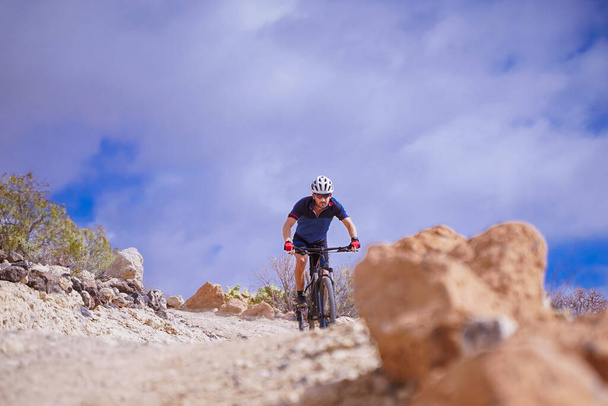 Ποδηλάτης με μπλε t-shirt Οδηγώντας ένα ποδήλατο βουνού. Ο άνθρωπος με το ποδήλατο βουνού κάνει βόλτες στο μονοπάτι μια τέλεια μέρα. Extreme Sport Concept - Εικόνα - Φωτογραφία, εικόνα