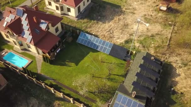 Aerial view of a private house with green grass covered yard, solar panels on roof, swimming pool with blue water and wind turbine generator. - Footage, Video