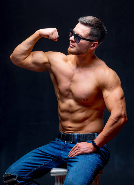 Portrait of a athletic muscular bearded man posing on a black background. Male in glasses showing muscles. - Fotó, kép