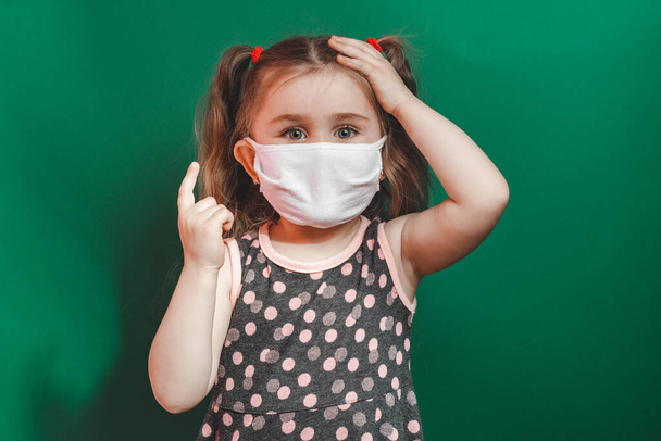 Conceptual photo of little girl in medical mask showing pointing finger on green background close up 2020 - Photo, Image