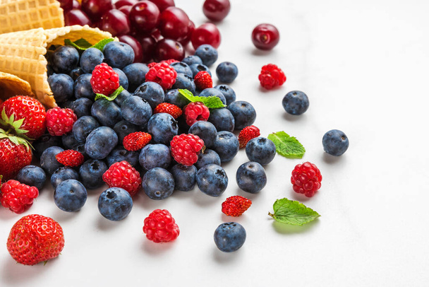 Βατόμουρα, σμέουρα, φράουλες και μούρα κεράσι σε χωνάκια παγωτού βάφλας σε λευκό μαρμάρινο τραπέζι. Έννοια θερινών τροφίμων - Φωτογραφία, εικόνα