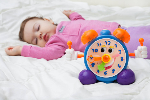 Children's alarm clock on the background of a sleeping child. Baby Day Mode Concept Photo - Photo, Image