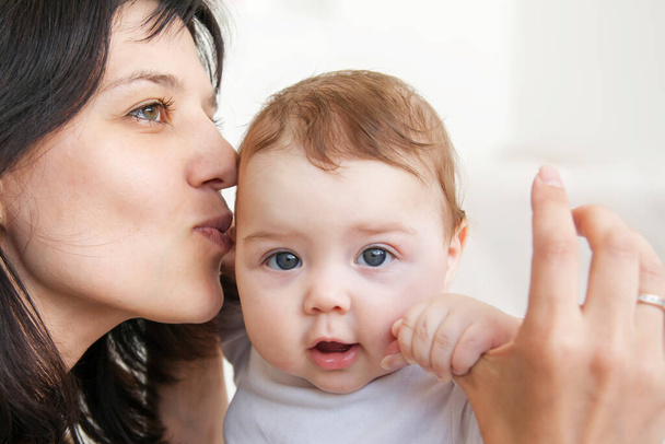 Mom kisses the infant who holds her hand. Motherhood and love concept - Photo, Image
