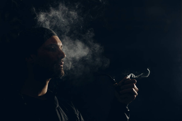 Man smoking a pipe on dark background. Profile portrait. - Фото, зображення