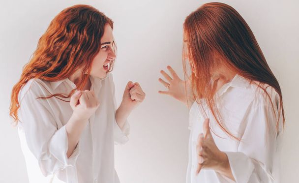Zwei rothaarige Schwestern stehen isoliert auf weißem Grund in großzügigen, überdimensionalen Hemden. Zwei junge Frauen wurden wütend und schreien sich an. Sie empfinden Wut, Aggression, Wut - Foto, Bild