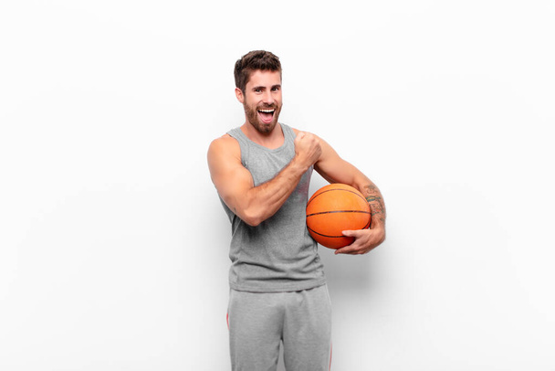 young handsome man feeling happy, positive and successful, motivated when facing a challenge or celebrating good results holding a basketball ball. - Foto, immagini